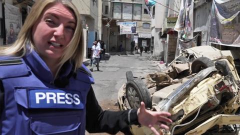 Middle east correspondent Anna Foster, next to an overturned car