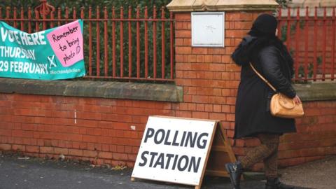 A woman walks past a polling station sign as voting begins in the Rochdale Parliamentary by-election near Manchester