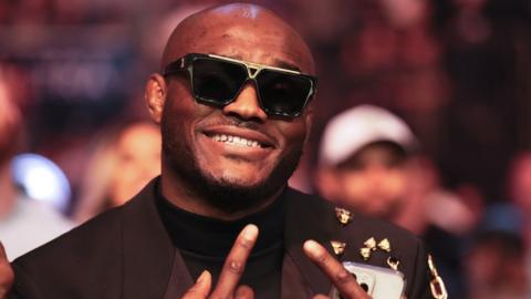 Kamaru Usman in shades and suit pulls face at camera