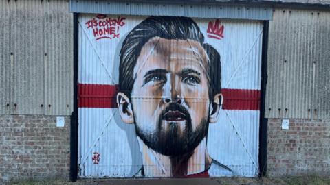 A picture of Harry Kane's face, with a St George's flag as the background, on a big corrugated metal door.