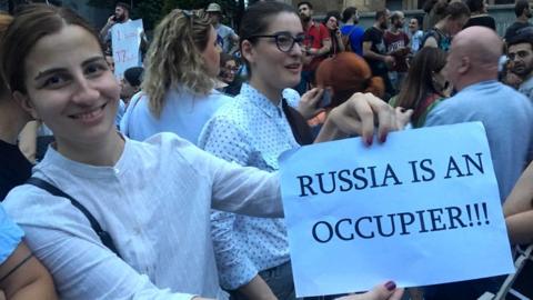 A protester holds up a piece of paper accusing Russia of occupying Georgian lands