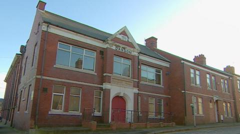 A large two-storey red brick building with a red door. It says "1910, Dawdon" on its front.