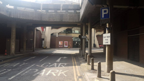 The entrance to the Broad Street Mall car park in Reading, with a blue sign with a white P in it on the right side and a sign that says "car park this lane" and directions on the road.
