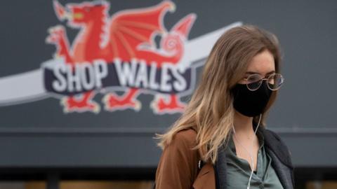 Woman in face mask with dragon on shop behind her in Cardiff