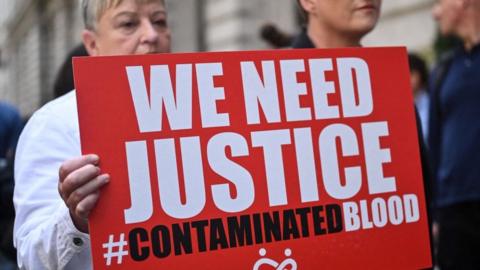Protestors hold placards with message related to the NHS infected blood scandal as Prime Minister Rishi Sunak gives evidence to the Infected Blood Inquiry in London, on 26 July, 2023