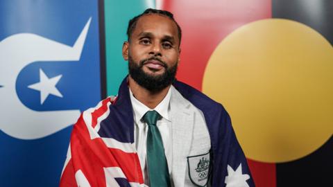 Australia's Olympic flag bearer Patty Mills posses in front of the Torres Strait and Aboriginal flags