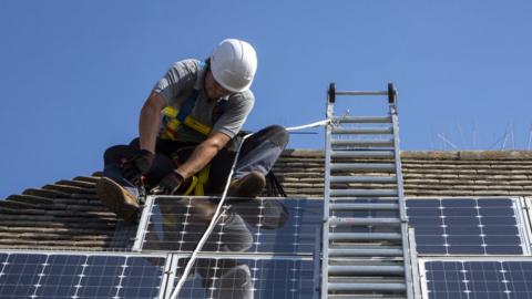 Man installing solar panel on roof of house