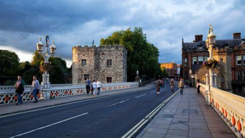A view of the road crossing Lendal Bridge in York. With iron work on either side of the footpaths with symbols of City of York and the initials V & A in red in places honouring honouring Queen Victoria and her husband Prince Albert