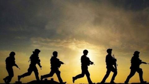 A photograph of silhouettes of soldiers walking against a sky backdrop
