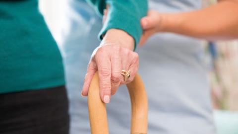 Carer supporting person walking with a stick