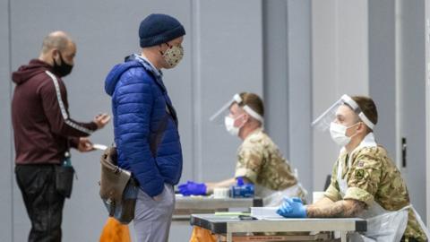 Two men talk to soldiers as they await test results