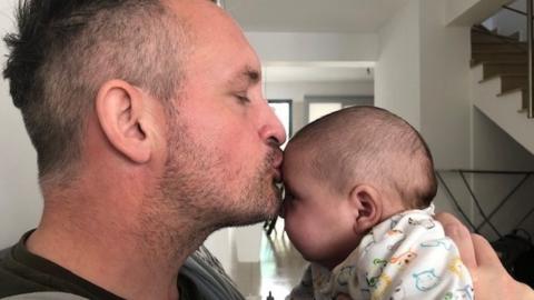 Joseph Taylor kissing baby Jonah on the forehead