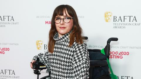 Lisa Hammond in the Winners Room at the BAFTA Television Craft Awards 2023. She is wearing a black and white jacket in a hounds tooth pattern and glasses and is using a wheelchair. 