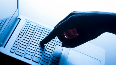A stock image of a person's hand on a keyboard in a dark room.