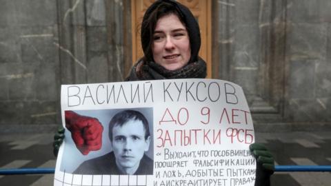 A protester stands outside an FSB office holding a photo of one of the convicted Set members