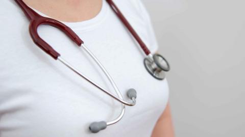 A close-up of a woman wearing a white T-shirt with a stethoscope around her neck.