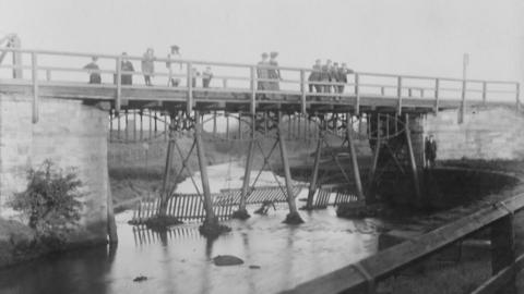 An old black and white picture of people standing on the bridge