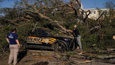A law enforcement officer cuts a tree with a chainsaw to free a trapped police vehicle after thunderstorms spawning high straight-line winds and tornadoes ripped across the state in Rolling Fork, Mississippi