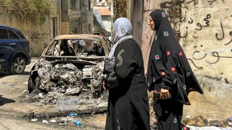 Locals inspect the damage to their homes and property seen here by two women close to a burnt out car