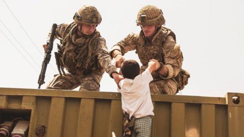 Western troops help a child climb into Kabul airport in August