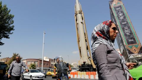 A woman walks past a Shahab-3 ballistic missile and launcher on a street in Tehran, Iran, during Defence Week (26 September 2019)