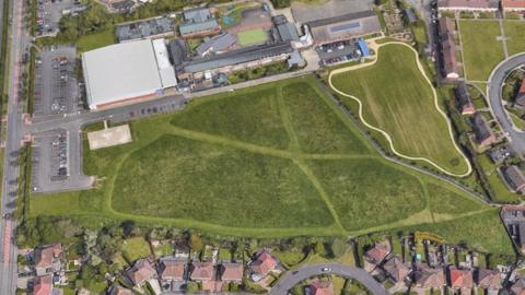 Aerial picture of green field surrounded by houses and next to a community centre