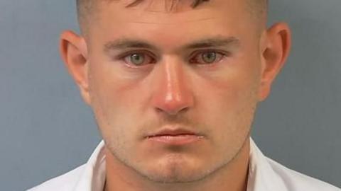 A police "mugshot" photo of Stephen Rennie. He is clean shaven, has dark hair and green eyes. He is wearing a white shirt.