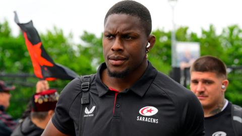 Maro Itoje wearing a black Saracens top looks on with a straight face
