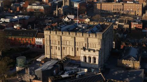 A Norman castle stands on a mound in a city centre surrounded by buildings