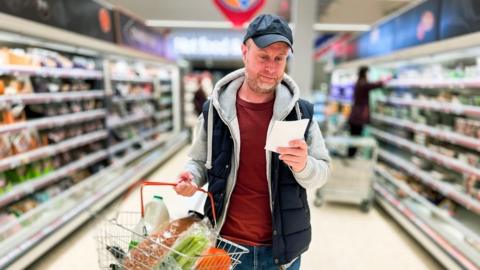 Man looks a shopping list as he walks through a supermarket aisle