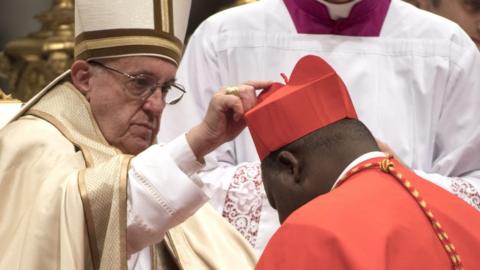Pope Francis (L) places the red three-cornered biretta hat on the head of new Cardinal Dieudonne Nzapalainga (R), Archbishop of Bangui in The Central African Republic - 19 November 2016