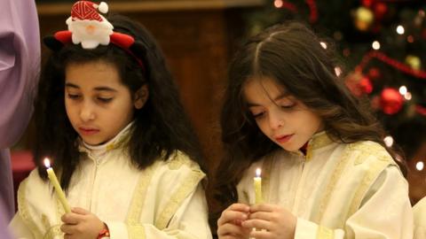 Two children taking part in a mass ceremony in Damascus, holding a candle