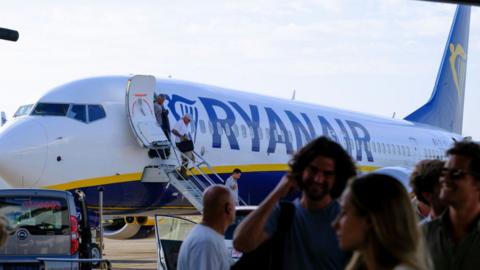 Passengers on the tarmac at an airport waiting to board a Ryanair aeroplane.