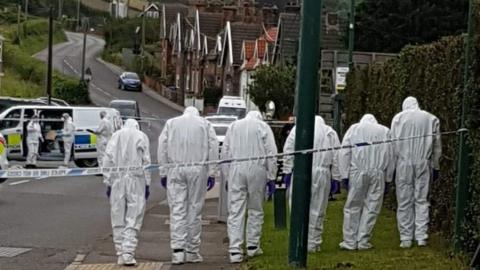 Forensic teams wearing white suits at the scene