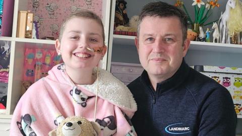 Megan in a pink onesie with a teddy next to her dad Matt who is wearing a navy top with a zip at the neck