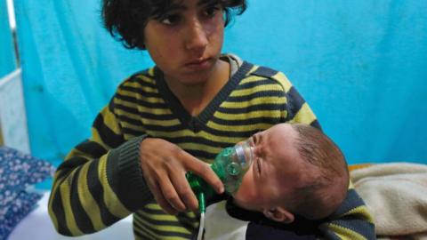 A Syrian boy holds an oxygen mask over the face of an infant at a make-shift hospital following a reported gas attack on the rebel-held besieged town of Douma in the eastern Ghouta region on the outskirts of the capital Damascus on 22 January 2018