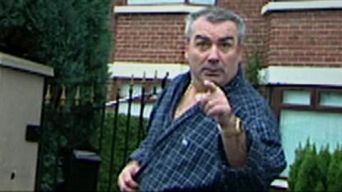Freddie Scappaticci pointing at the camera with his eyebrows raised. Semi-detached houses and a hedge are visible behind him.