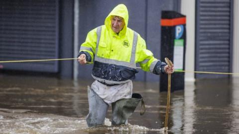 A man wearing a fluorescent coat wades through floodwater in Newry