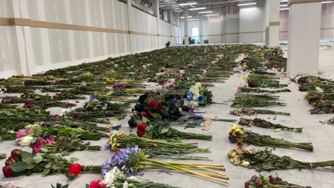 Rows of hundreds of bouquets of flowers laid out on the concrete floor of a warehouse.