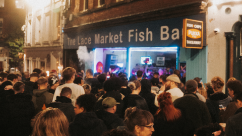 A crowd of people taken from behind them, standing outside fish bar in Nottingham city centre while a rave happens inside