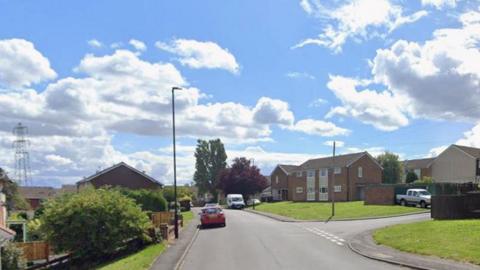 Dawson Avenue in Rawmarsh, which includes housing on both sides of the road and a number of cars parked. The sky is blue with some cloud cover.