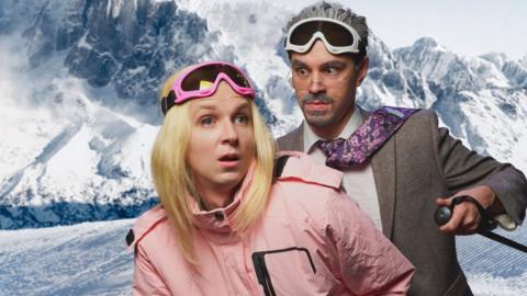 Two people in front of a snowy mountain background. In the Front, actor Linus Karp wears a blonde, shoulder-length bob wig, with a pair of pink-rimmed ski goggles on his forehead. He's wearing a pink, whole-body ski suit with black accents on the shoulders and pocketeer on the left breast. He's sporting a vacant expression as he looks off into the distance. Behind him, actor Joseph Martin wears a fake grey goatee beard, glasses and has grey hair combed back. He wears white-rimmed ski goggles and a grey-brown suit with a white shirt. His purple tie with pink floral pattern is flicked back over his shoulder, showing the underside of the tie. He's looking intensely at Linus with an angry face.