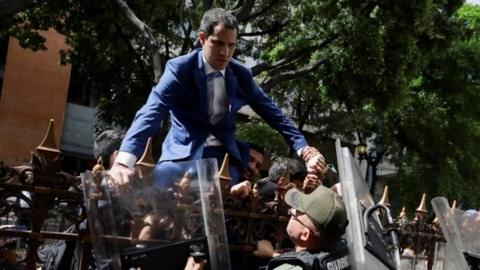 Venezuelan opposition leader Juan Guaido climbs a fence in an attempt to enter the headquarters of the National Assembly