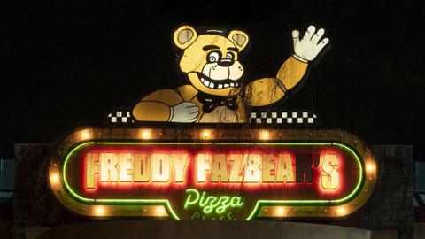 A slightly grubby neon sign that reads "Freddy Fazbear's Pizza" in block capital letters. Above the lettering is an illuminated bear character. He's smiling and has one arm raised in a wave.