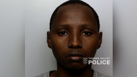 A mugshot of Edwine Kiplangat, who is expressionless and wearing a grey T-shirt.