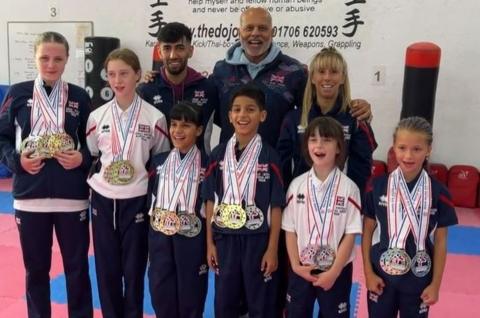 Six children stand in front with their karate medals while three teachers stand behind them smiling