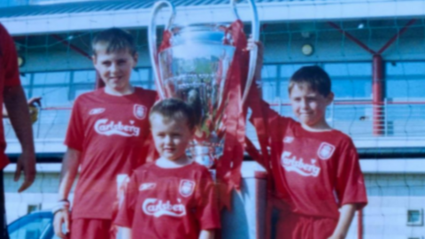 Accrington Stanley forward Josh Woods (front) aged five in his Liverpool kit with the 2005 Champions League trophy with his brothers Connor (right) and Dale (left)