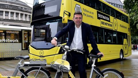 Andy Burnham poses with bike, bus and tram