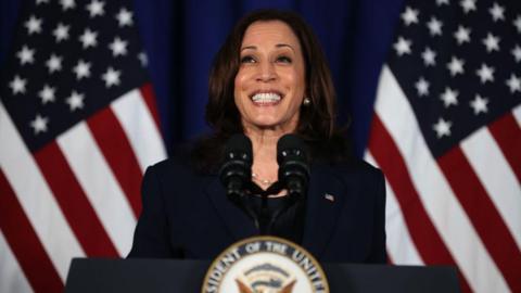 Kamala Harris, wearing a deep blue blazer and blouse, smiles as she delivers remarks at the Louis Stokes Library on the campus of Howard University in 2021