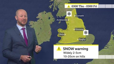 Darren Bett stands in front of a weather map of the UK showing a yellow snow warning